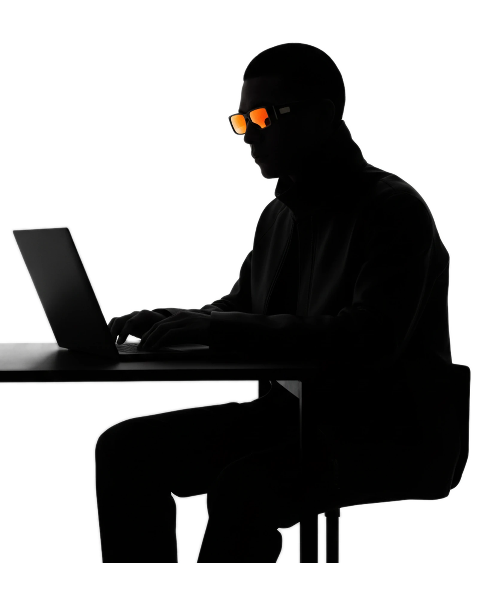 Near-black silhouette of a person typing at a laptop, wearing signal-orange glasses